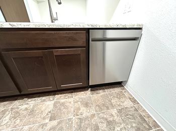A kitchen with a stainless steel dishwasher and brown cabinets